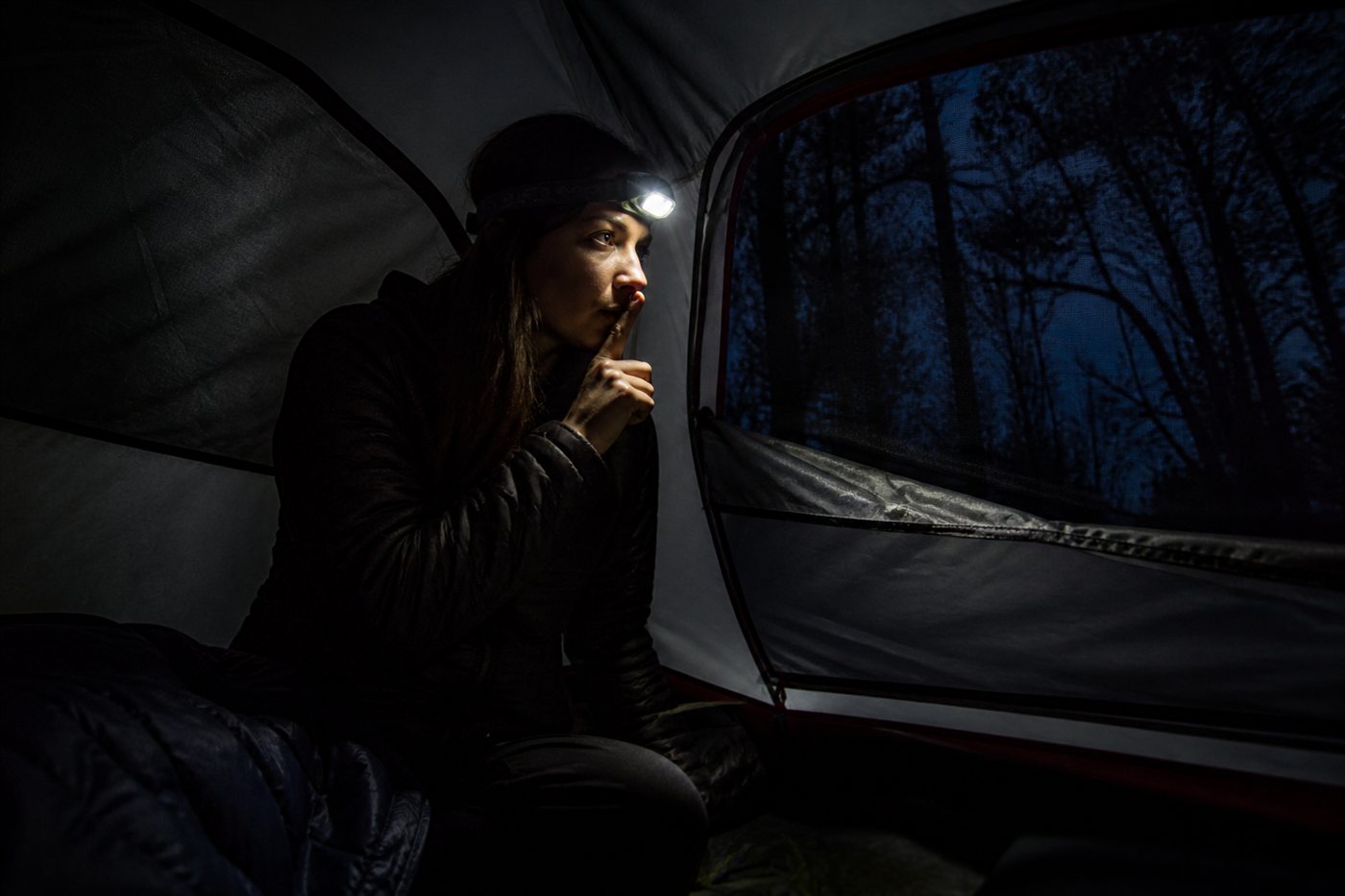 Solo camper listening inside her tent at night, hand raised for silence