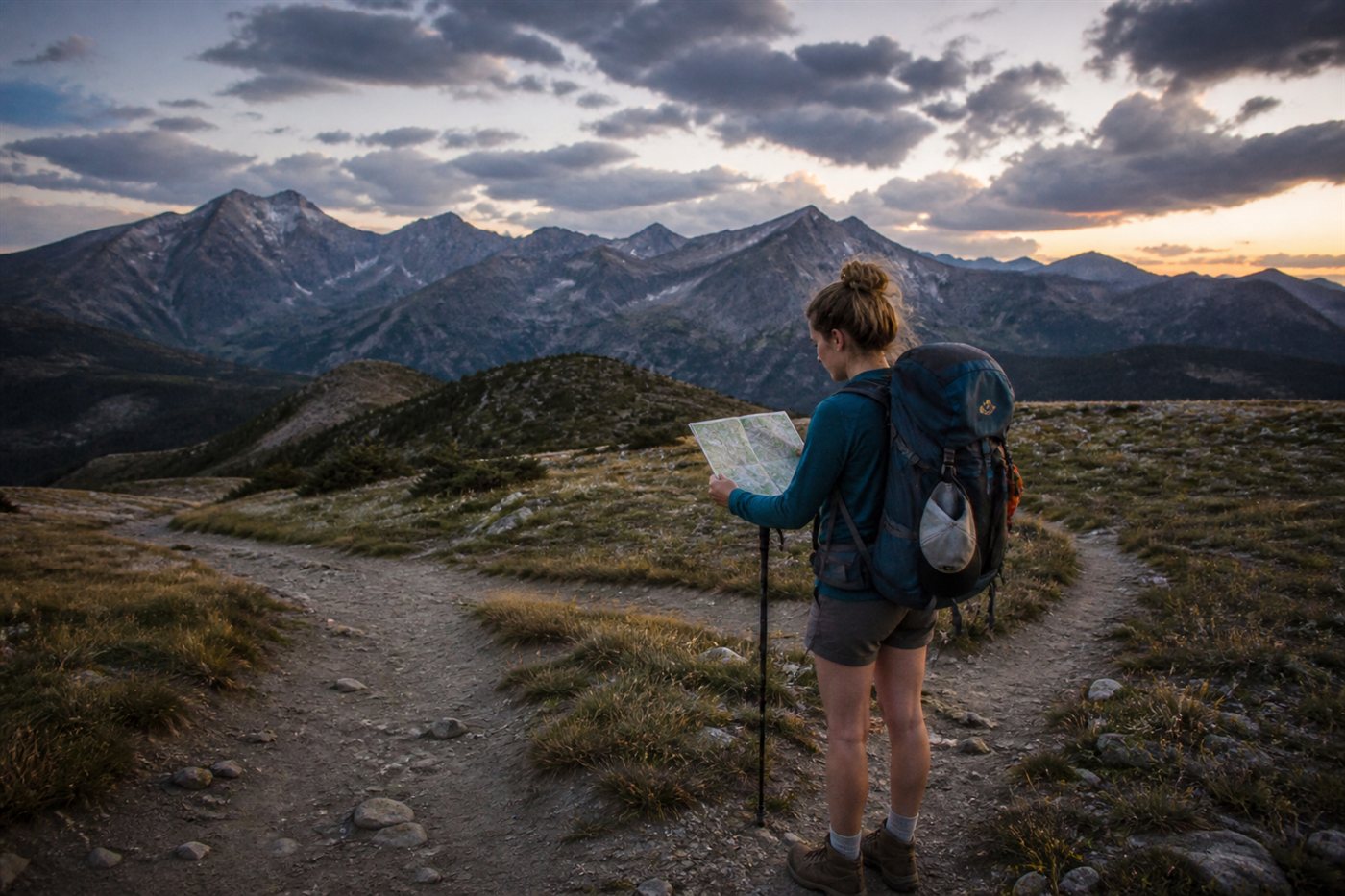 Backpacker studying a paper map at an unmarked trail fork at dusk